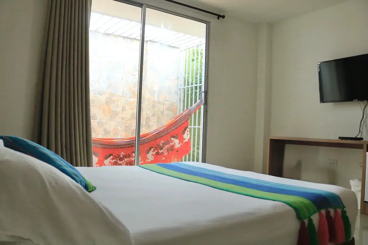 Habitación de Emerawaa con cama doble, cubrecama de colores y hamaca guajira en el patio