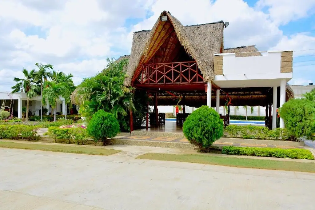 Kiosco de techo de palma junto a la piscina, rodeado de palmeras y jardines