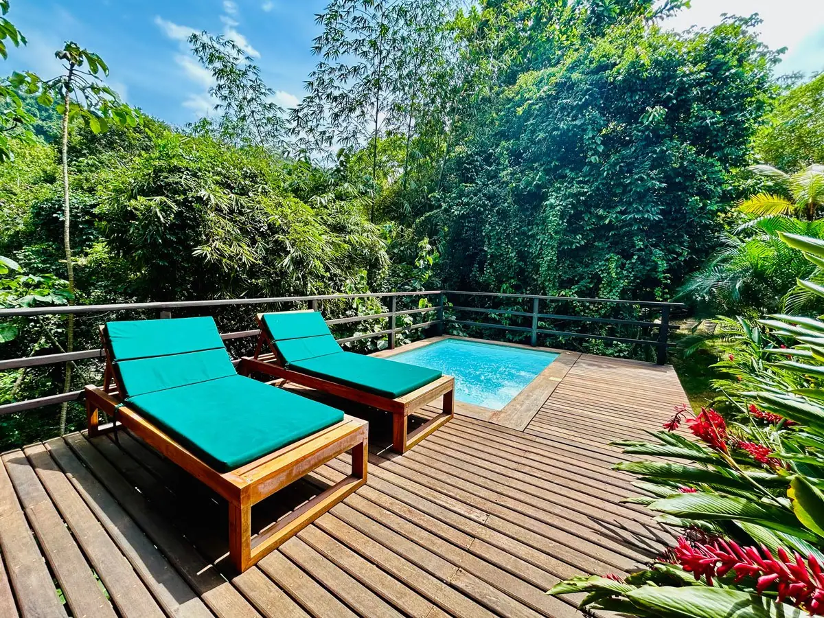 Terraza de madera con asoleadoras y piscina privada frente a la selva en Senda Watapuy
