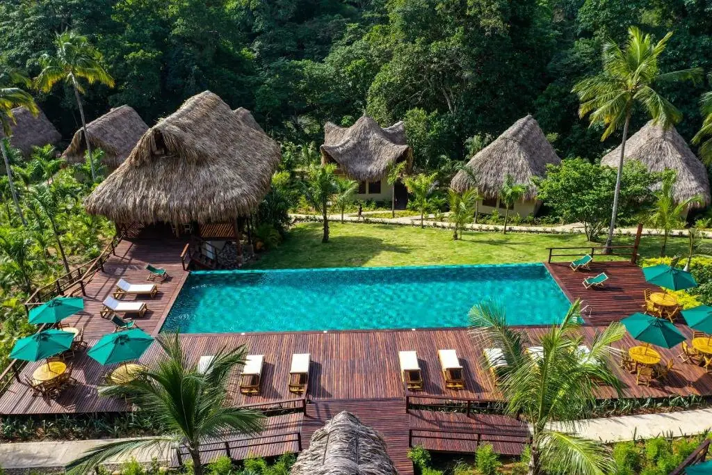 Piscina de Senda Watapuy con cabañas de techo de palma y montañas al fondo