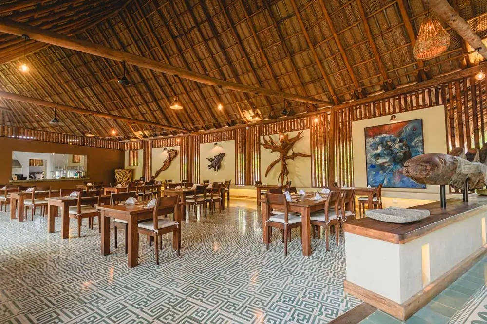 Restaurante de Senda Watapuy con techo de palma, mesas de madera y piso de baldosa