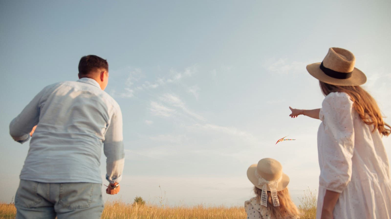 Papá, mamá e hija volando una cometa en el campo al atardecer