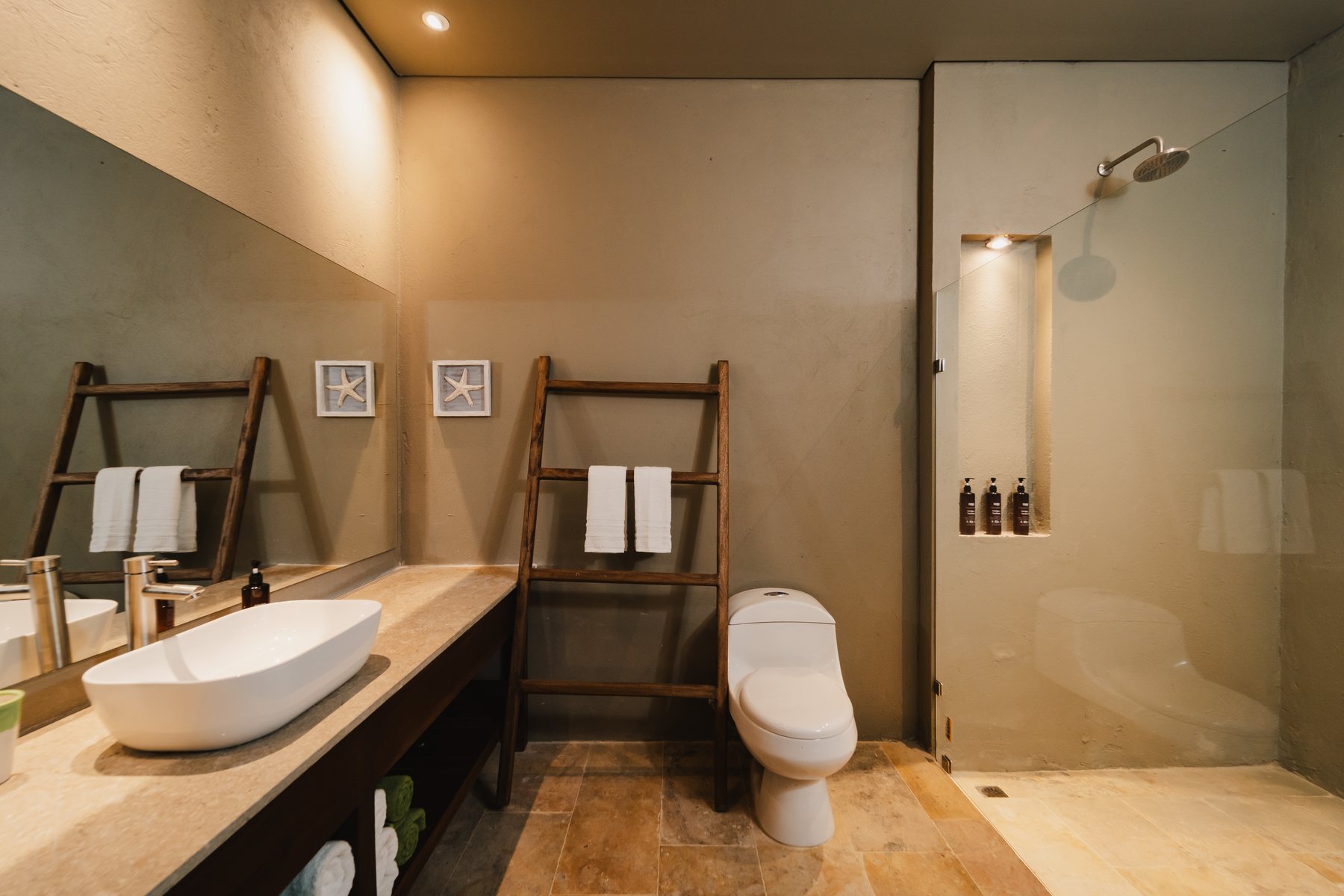 Baño de Naio con lavamanos de piedra, ducha y toallero de madera