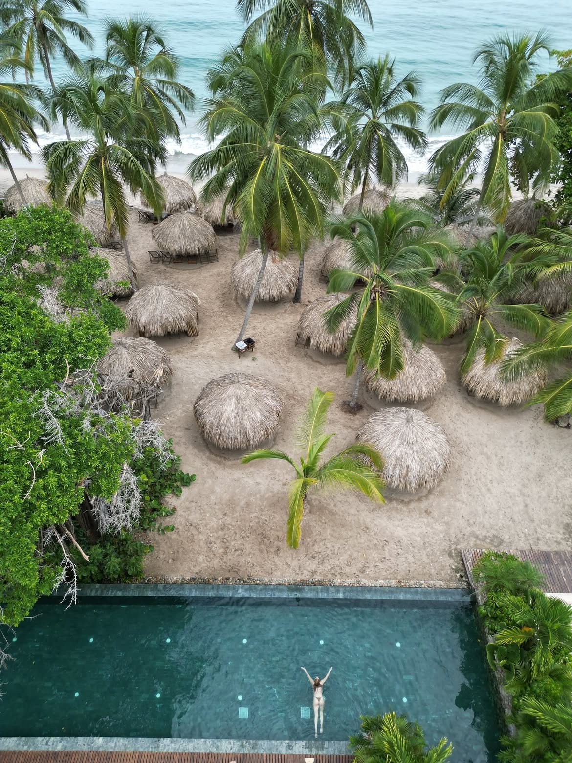 Piscina de Naio rodeada de palmeras y palapas junto a la playa