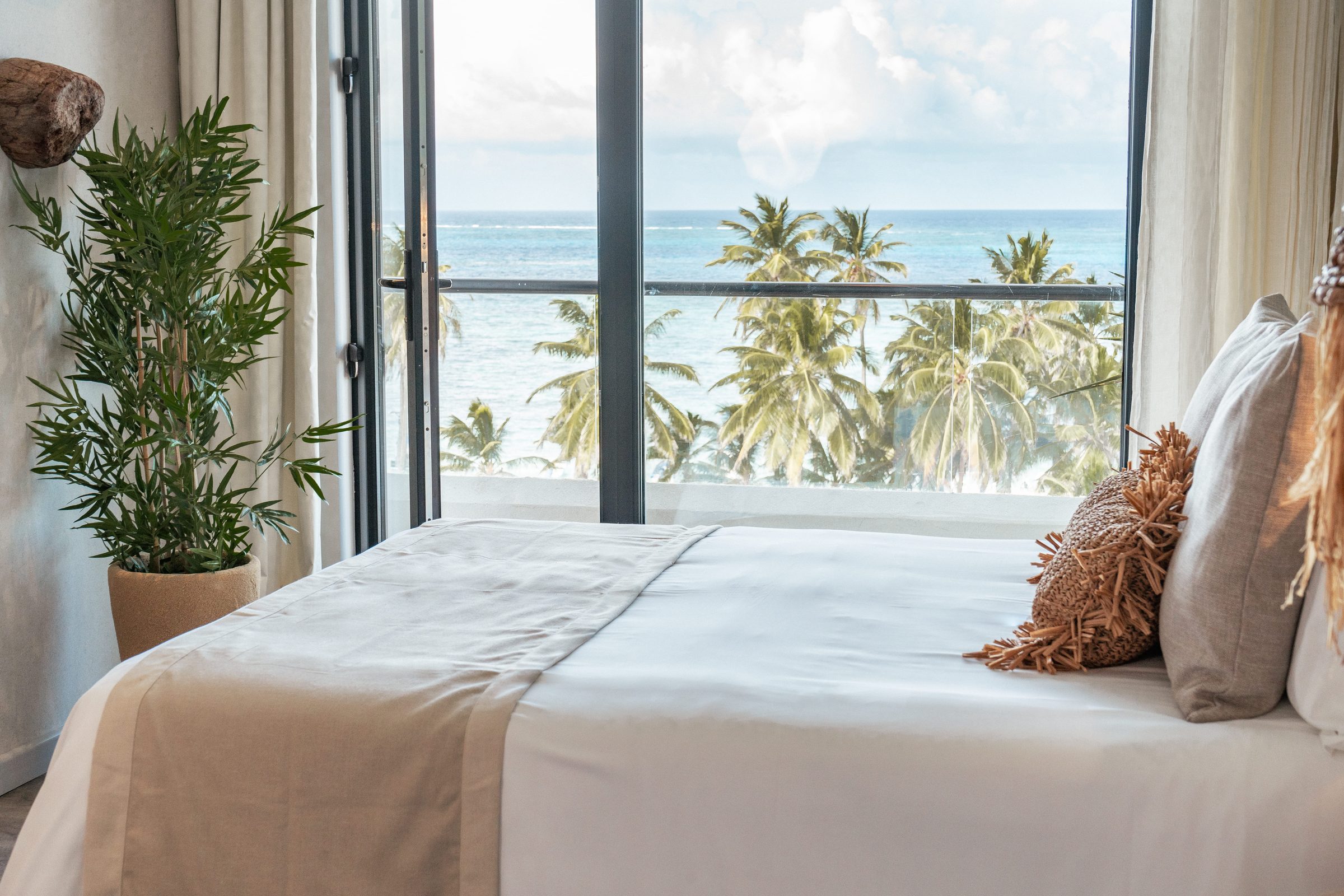 Habitación Superior de Nattivo con cama blanca, palmeras y el mar de San Andrés en el ventanal